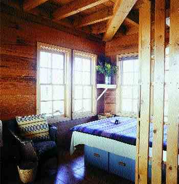 
Most mornings begin with coffee in the middle-floor bed where Glenda and Dick can watch dawn light up the mountains and birds arrive at the feeder. Dick built the queen-size bed on a box with drawers for ten cubic feet of storage. The beams, floor, and wallboards are recycled wood. The built-in, multi-shelved headboard and window casings come from a local pine mill’s over-runs.
